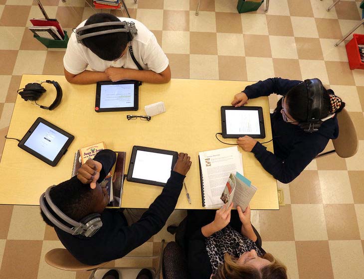 Students sitting around a table reading their tablets